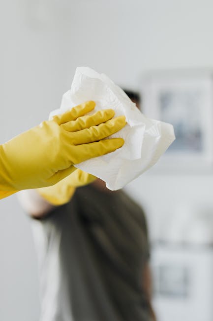Two professional cleaners from cleaners-finchley.com dressed in beige uniforms with white accents, standing indoors against a plain white wall, holding cleaning tools. The cleaner on the left is holding a red vacuum cleaner, while the cleaner on the right is holding a green mop. The surface area appears clean and well-maintained, suggesting thorough domestic or commercial surface cleaning, including floor and window glass sanitisation. The lighting in the room is bright and natural, highlighting the shiny, dust-free floors and the tidy appearance of the cleaners' uniforms, indicative of a high standard of hygiene and deep cleaning processes provided by [COMPANY_NAME], as detailed on the 'Same Day End of Tenancy Cleaning North Finchley N12, Finchley' page.
